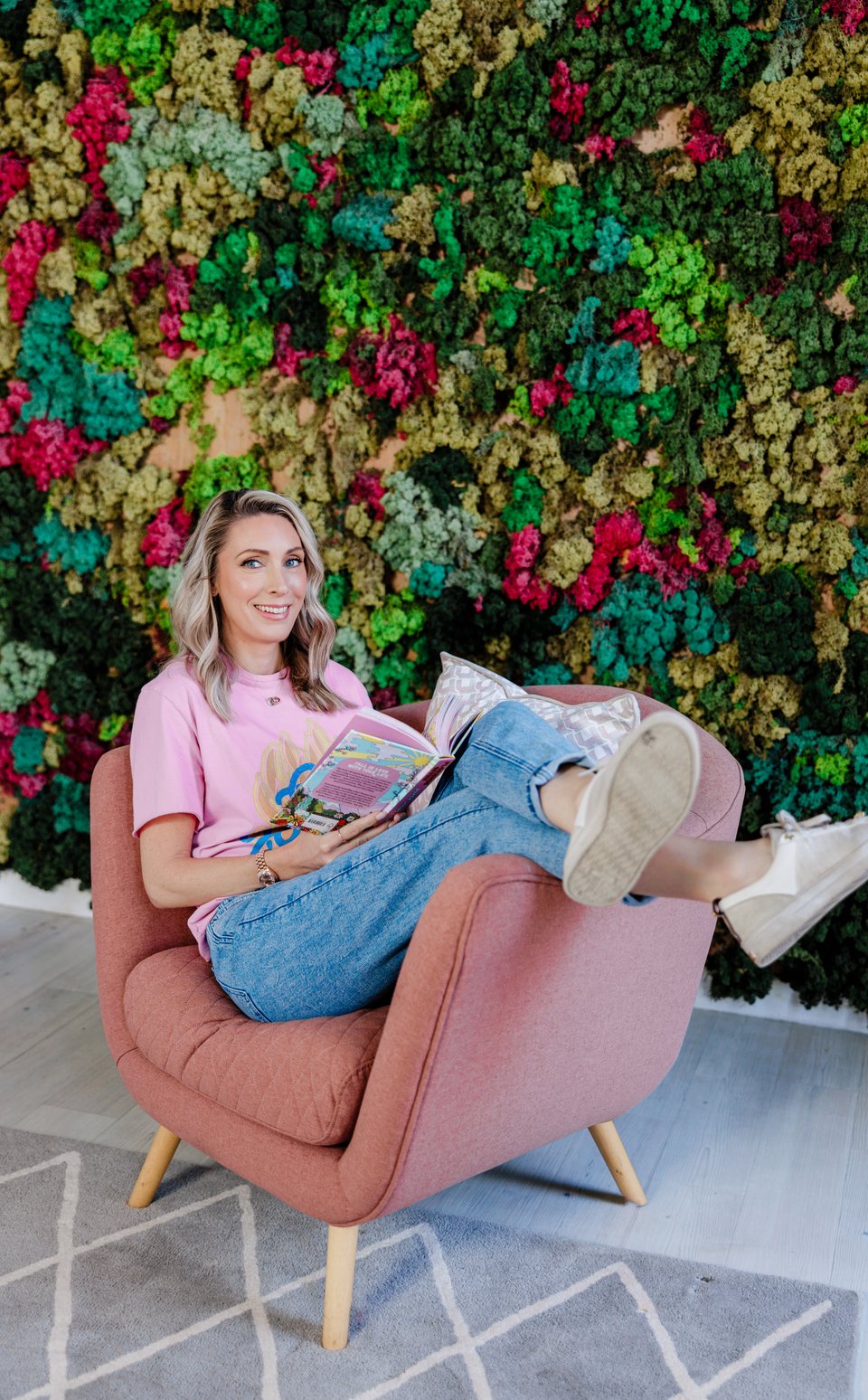 Carrie Green smiling in a pink armchair with a book